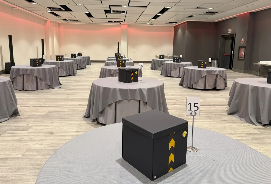 Escape room para grupos numerosos: salón de hotel con mesas redondas y una caja de juego en cada una